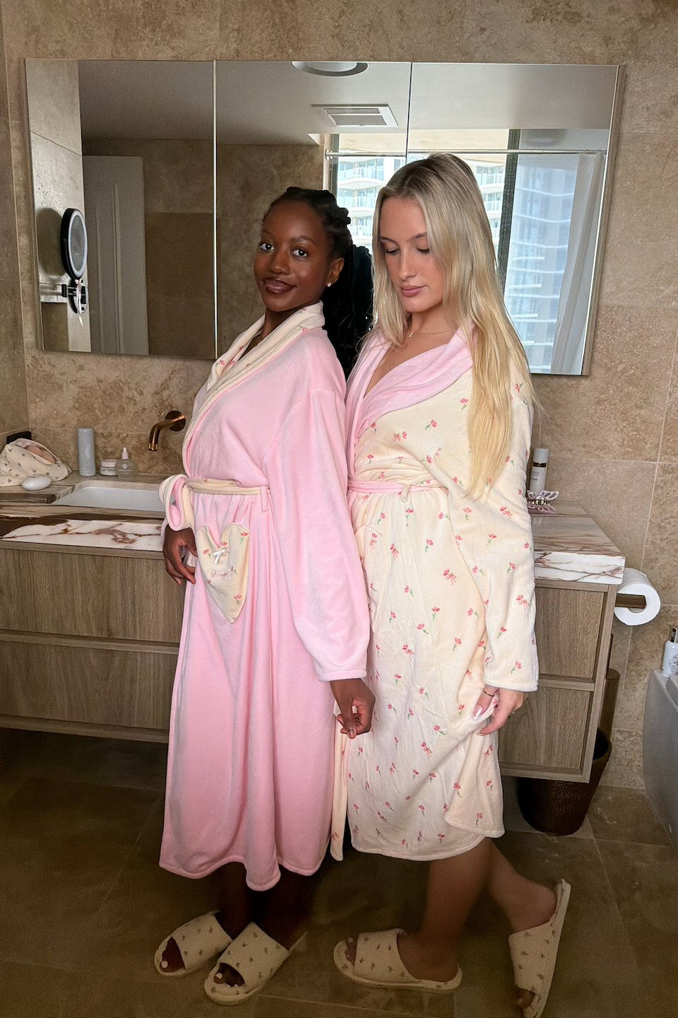 Two women in pink and white robes standing in a bathroom.