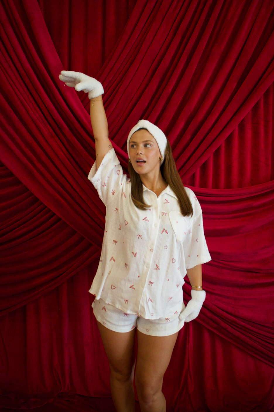 Brunette girl in a christmas pajamas with red patterns against a red curtain backdrop with snow gloves and headband